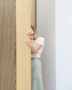 woman in white lace cap sleeved top and green skirt hiding behind brown wall