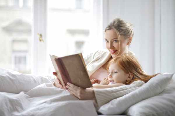 woman and a girl on bed holding a book